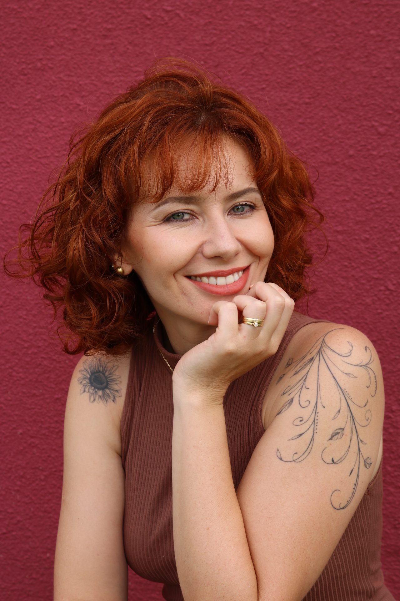Dayana Barrussi, psicóloga clínica, sorrindo diante de uma parede vinho